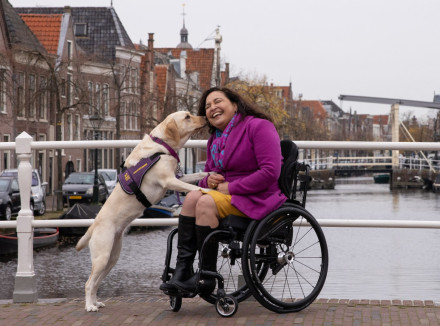 vrouw in rolstoel buiten op een brug krijgt een lik van haar assistentiehond